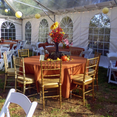 Table and chairs set up under an event tent outside