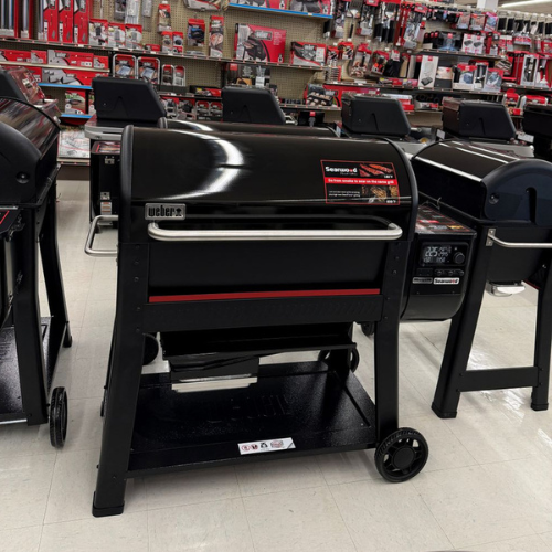 Display of black Weber grills in a hardware store, showing multiple units with red accents. The setting is organized and well-lit, suggesting a professional retail environment.