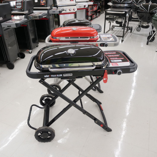 Portable grills displayed in a store, with sleek black and red designs on folding stands. The setting suggests a focus on outdoor cooking equipment.
